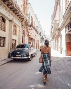 a woman walking down the street in front of an old car