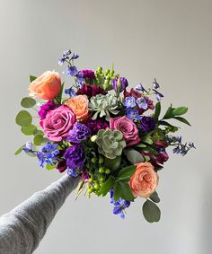 a bouquet of flowers being held up by a person's hand in front of a white wall