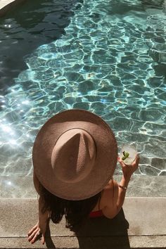 a woman sitting on the edge of a swimming pool holding a drink in her hand