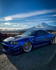 a blue car parked in front of a mountain with clouds and snow on the top