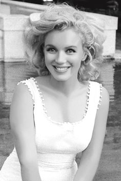 a black and white photo of a woman with blonde hair wearing a dress smiling at the camera