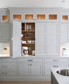 an open cabinet in the middle of a kitchen with white counter tops and cabinets on both sides