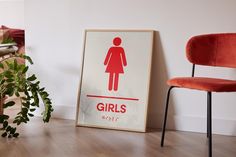 a red chair sitting next to a poster on the wall in front of a potted plant