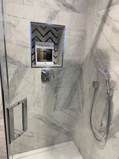 a bathroom with white marble walls and flooring, shower head, and hand rail