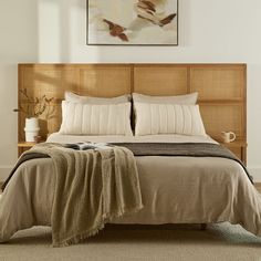 a bed with two pillows and blankets on it next to a painting hanging above the headboard