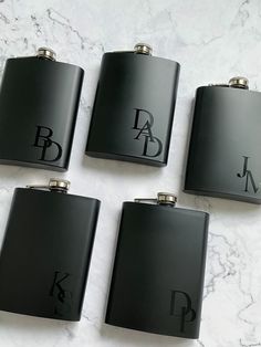 four black flasks with monogrammed letters on them sitting on a marble surface