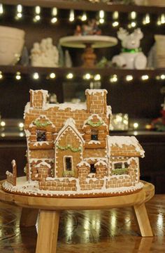 a gingerbread house is sitting on a wooden table in front of christmas lights and other holiday decorations