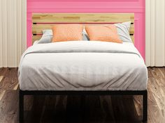 a bed with two orange pillows on it in front of a pink wall and wooden floor