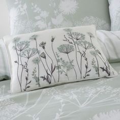 a bed with white and green floral designs on the pillowcase, along with two pillows