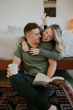 a man and woman sitting on top of a bed next to each other holding a book