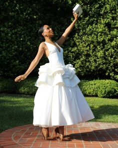 a woman in a white dress is holding her arms out to the sky while standing on a brick walkway