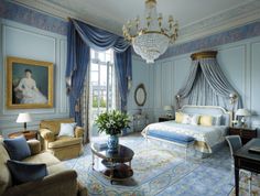 a bedroom with blue and white walls, chandelier, couches, chairs and paintings on the wall