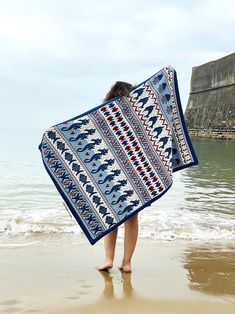 a woman is walking on the beach holding a blanket