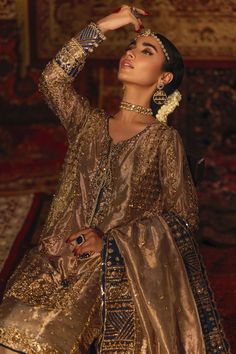 a woman in an elaborate gold dress poses for the camera with her hand on her head