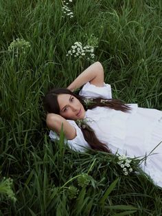 a woman laying in the grass wearing a white dress