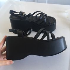 a person is holding up their black platform sandal wedges on a white surface