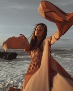 a woman standing on top of a beach next to the ocean holding an orange scarf