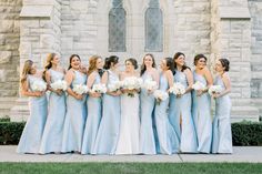 a group of women standing next to each other in front of a stone building holding bouquets