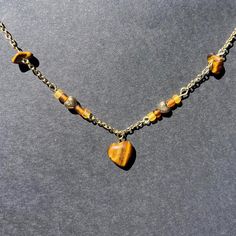 This handmade necklace features a delicate gold chain adorned with a striking heart-shaped, tiger's eye gemstone pendant with bead and gemstone accents along the chain. The warm, earthy tones of the tiger's eye stones add a natural elegance to this unique piece. Perfect for those who love boho and nature-inspired jewelry, this necklace complements any outfit with its rich colors and sophisticated design. The high-quality materials and craftsmanship make it a wonderful gift for birthdays, anniversaries, or any special occasion. Wear it alone for a subtle statement or layer it with other necklaces for a more bohemian look. This is a new shop so please don't be discouraged by the low amount of orders and reviews at this time. Feel free to reach out with any questions, comments, or concerns! Gold Necklaces With Heart Charm And Round Beads, Adjustable Gold Beaded Necklace With Heart Charm, Spiritual Heart Beads Pendant Necklace, Gold Heart-shaped Beaded Jewelry, Brown Heart-shaped Bohemian Necklace, Bohemian Brown Heart-shaped Necklace, Brown Bohemian Heart Necklaces, Gold Heart-shaped Beaded Necklaces, Gold Beaded Heart Necklace Gift