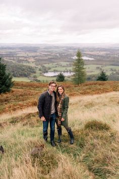 a man and woman standing on top of a grass covered hill