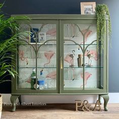 a green glass cabinet with flamingos on it and some plants in vases next to it