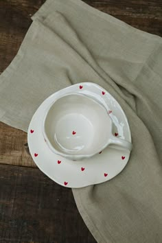 a white bowl with red hearts on it sitting on top of a wooden table next to a napkin