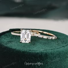 an emerald colored diamond ring sitting on top of a green velvet box