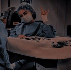 a woman in scrubs sitting at a table with her hand up to the camera