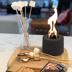 some marshmallows are sitting on a tray next to sticks and a candle