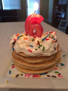 a stack of pancakes with a lit candle on top and sprinkles around it