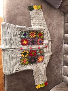 a crocheted sweater with flowers on it sitting on a couch next to a pillow