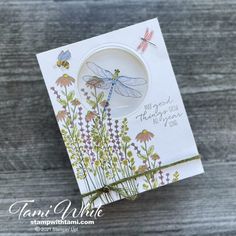 a card with a dragonfly on it and some flowers in front of the card