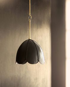 a black and white lamp hanging from a gold colored cord in a dark room with light coming through the window