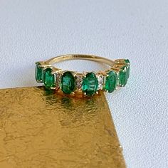 an emerald and diamond three stone ring on a gold plated surface with white background