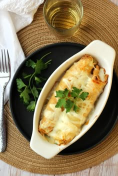 a black plate topped with an enchilada covered in cheese and cilantro