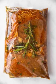 meat wrapped in plastic sitting on top of a white counter next to vegetables and herbs