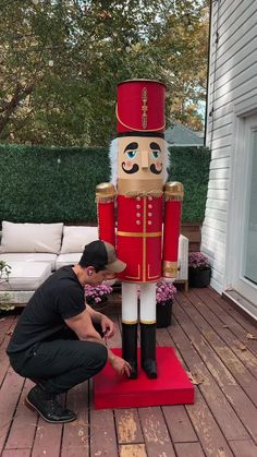 a man kneeling down next to a large nutcracker statue on top of a wooden deck