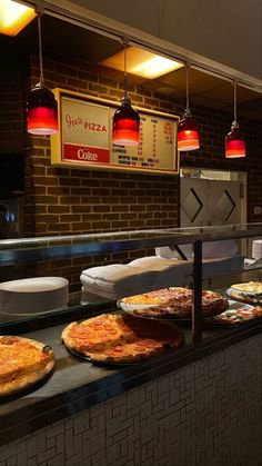 several pizzas sitting on top of a counter in front of a brick wall and lights