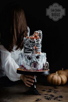 a woman holding a cake on top of a wooden table next to pumpkins and other decorations