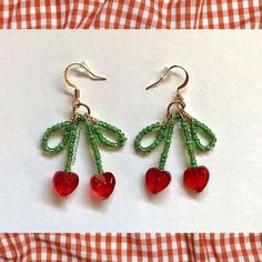 the earrings are made with beads and red heart shaped charms on them, sitting on a checkered tablecloth