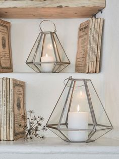 two glass lanterns with candles are on a shelf next to an old book and some books