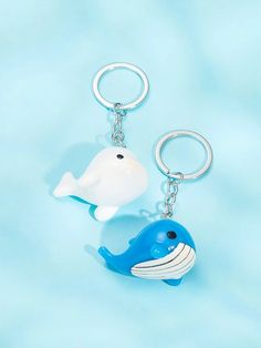 two keychains shaped like dolphins on a light blue background, one with a white tail and the other has a black nose