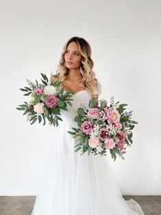 a woman in a white wedding dress holding a bouquet of pink and white flowers with greenery