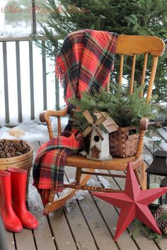 a wooden rocking chair sitting on top of a snow covered porch next to a christmas tree