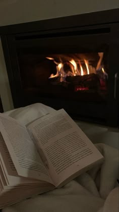 an open book sitting on top of a bed in front of a fire place filled with flames