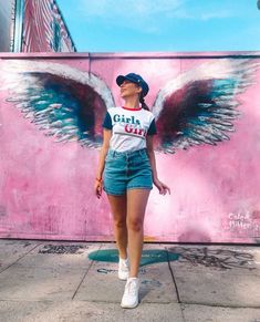 a woman standing in front of a pink wall with angel wings painted on the side