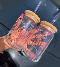 two pink tumblers with gold rims and glitter stars on them are being held by someone's hand