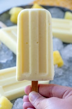 a hand holding a popsicle that is on top of ice and yellow cubes