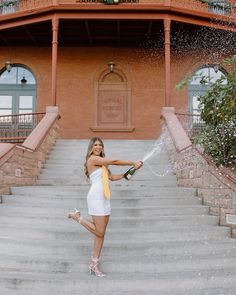 a woman in white dress spraying champagne on steps