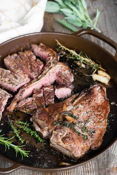 steaks in a skillet with herbs on the side